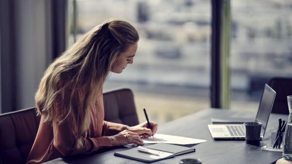 Woman writing at a desk with laptop