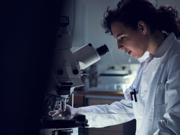 Woman in lab suit looking into a microscope