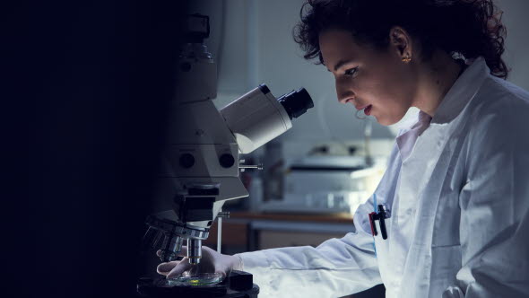 Woman in lab suit looking into a microscope